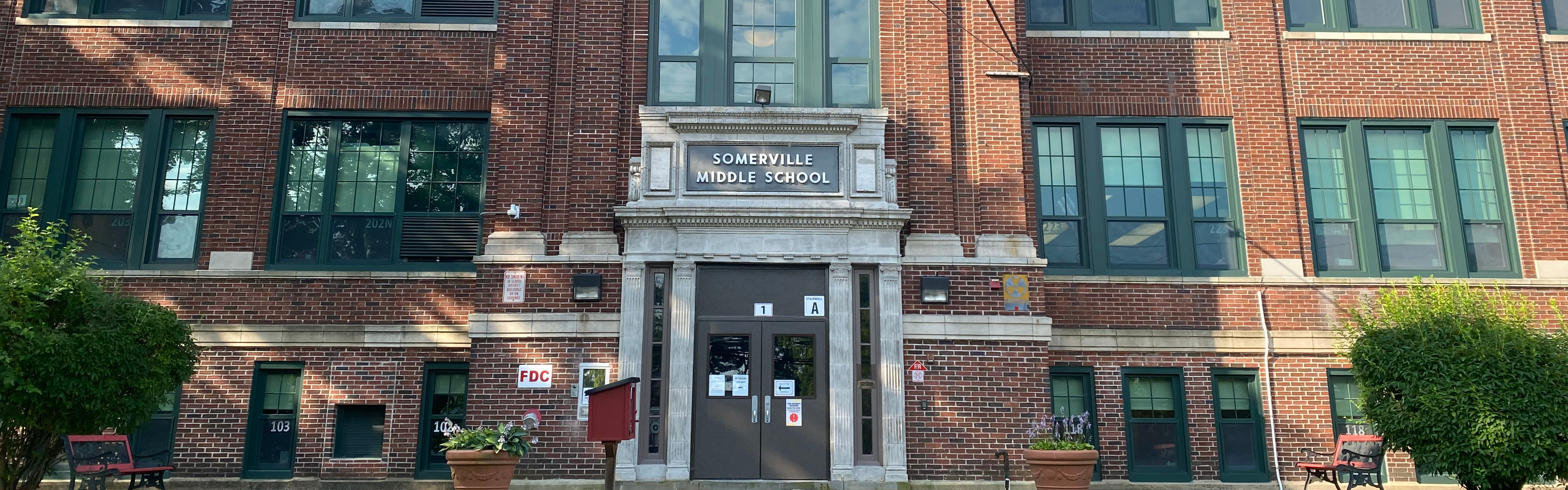 blue sky red brick building Somerville Middle School in white letters, green grass, beige sidewalk, brown front door