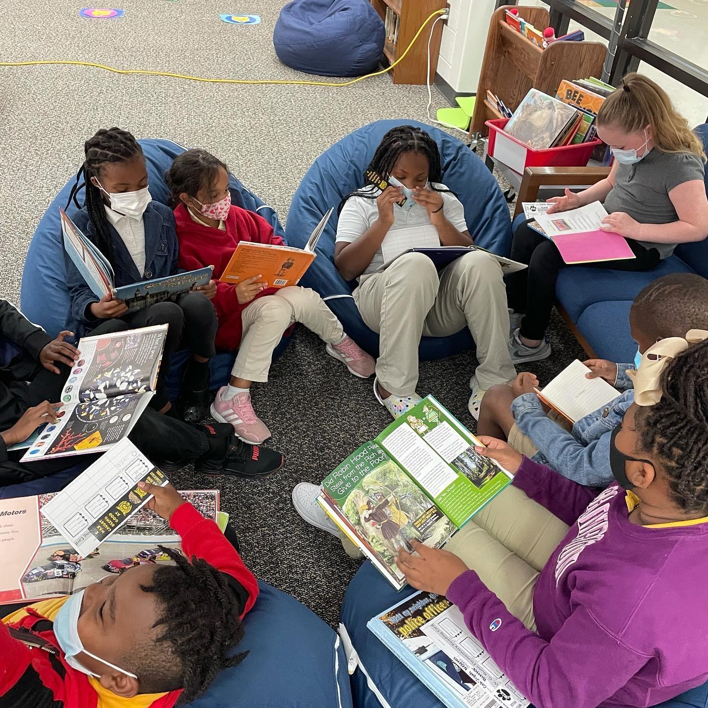 Students sitting on beanbag chairs in a circle reading books together