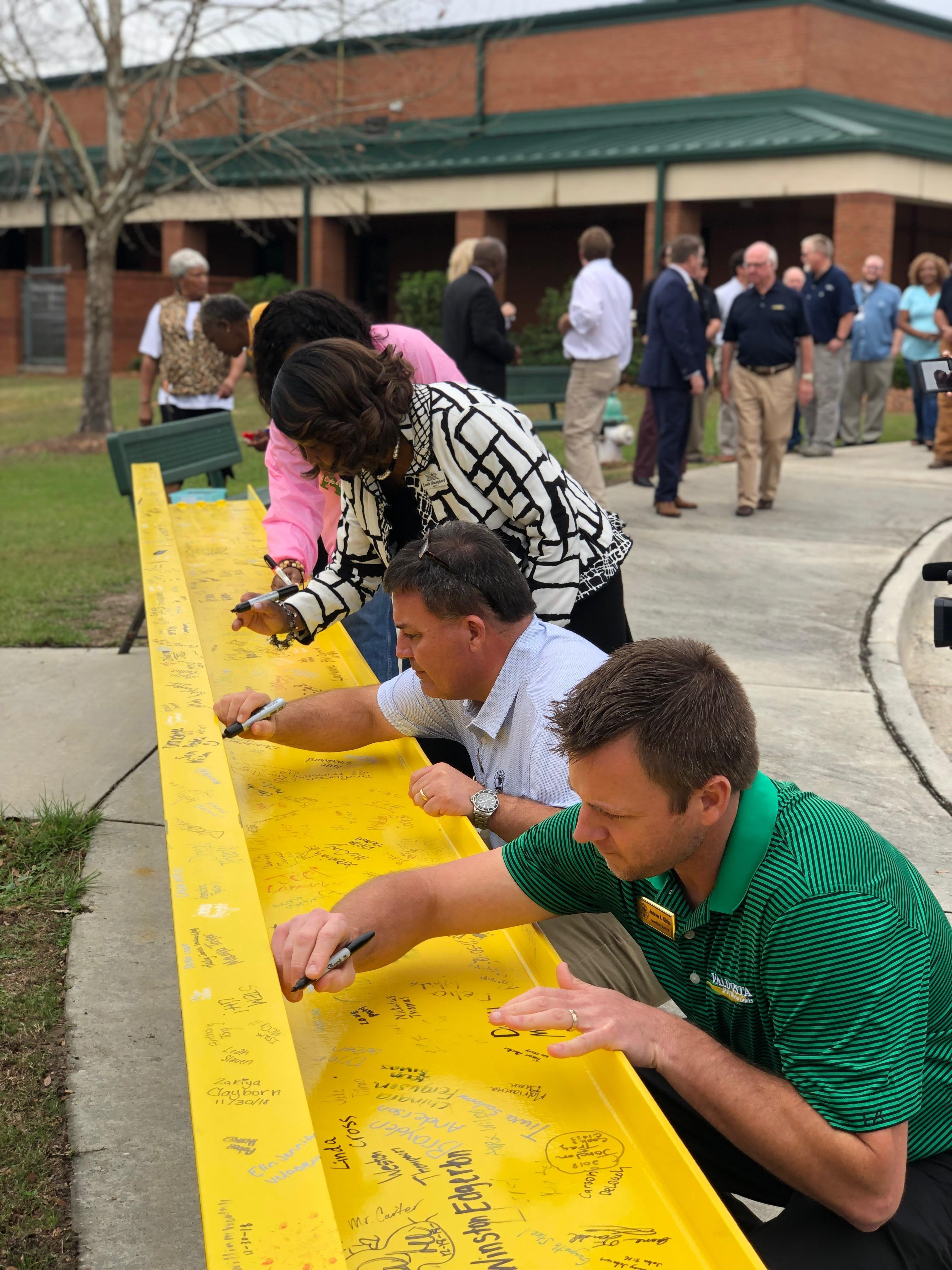 Line of people signing yellow bench