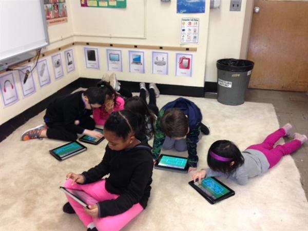 Six students sitting and laying on the floor working on tablets