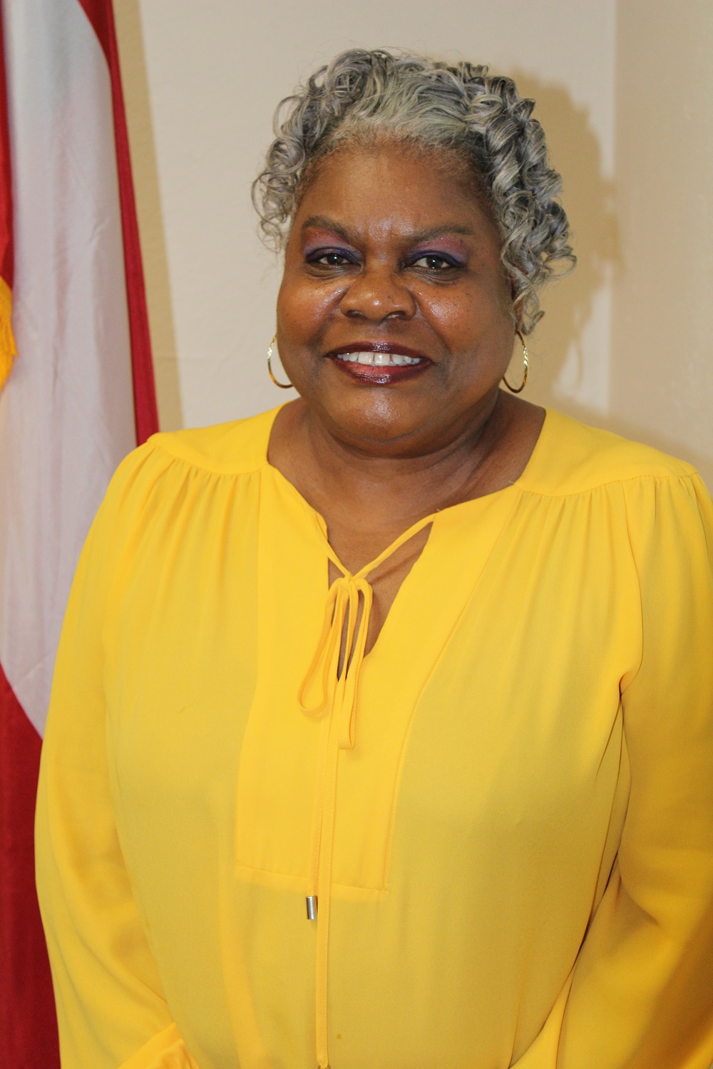 Sherrye Battle wearing bright yellow standing next to the flag