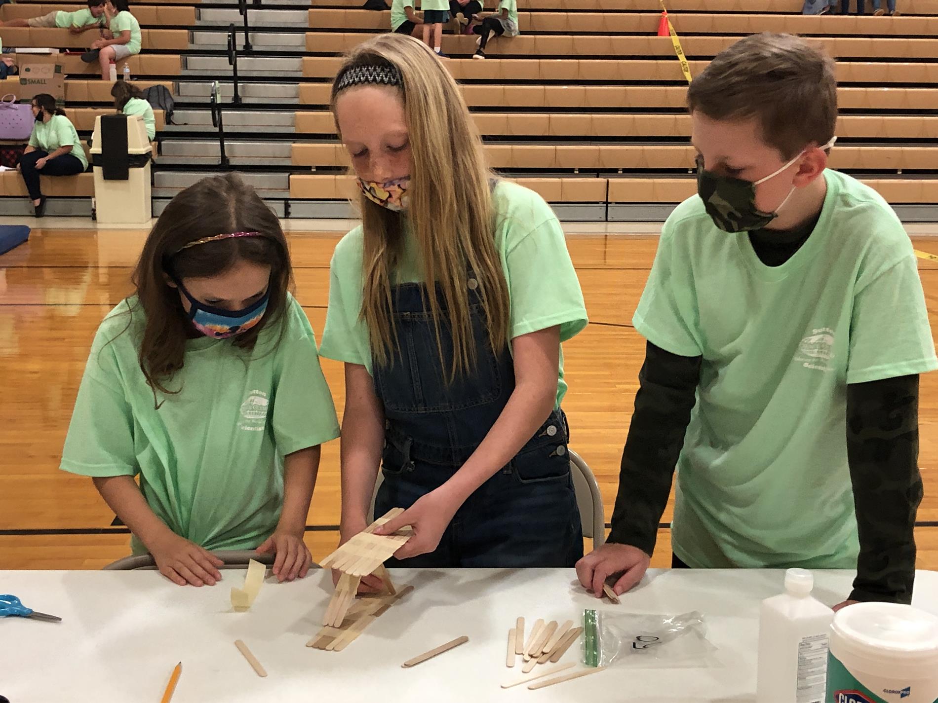 three students wearing green shirts building things out of paper