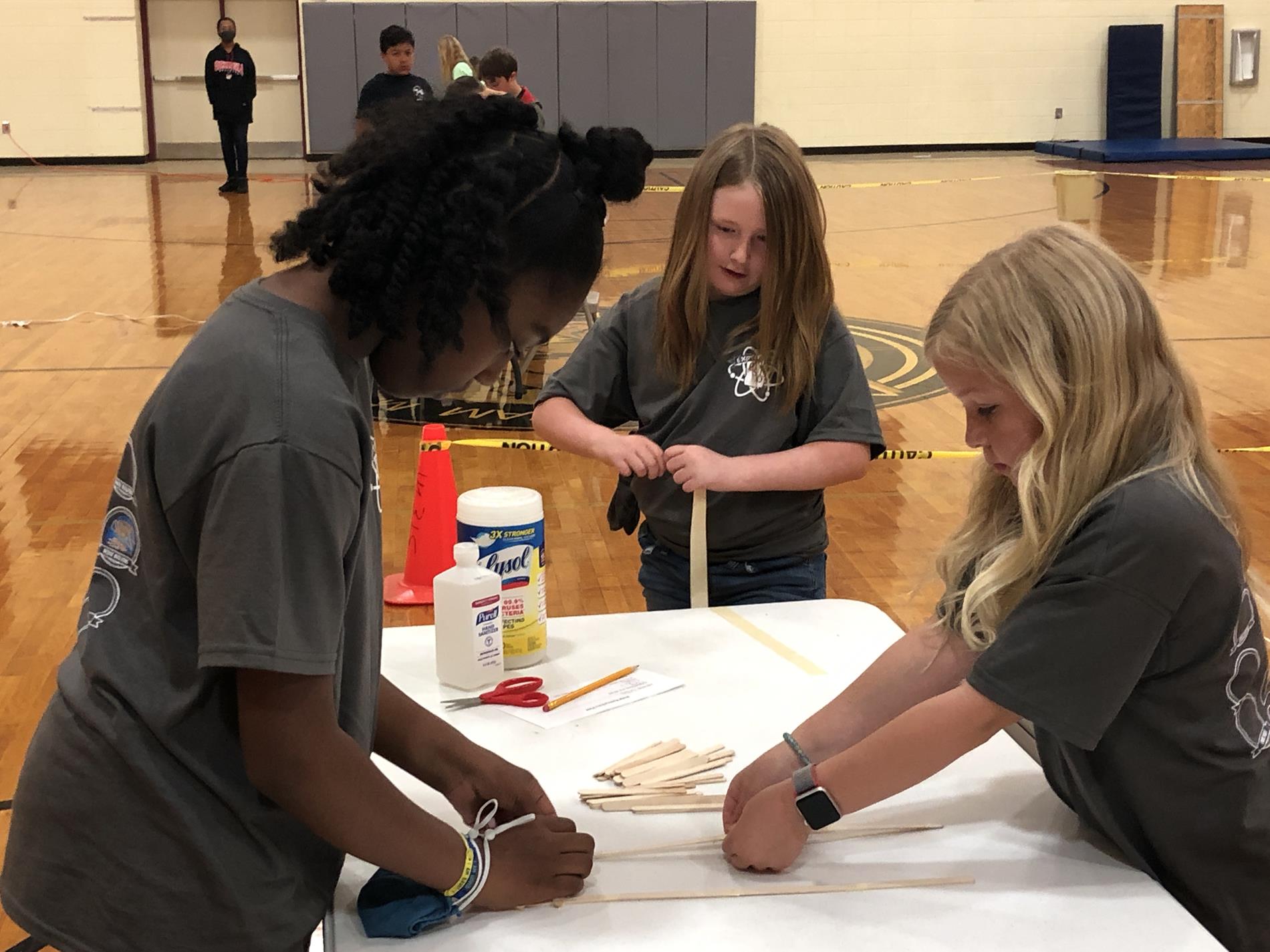 three students in grey shirts gluing small pieces of wood together
