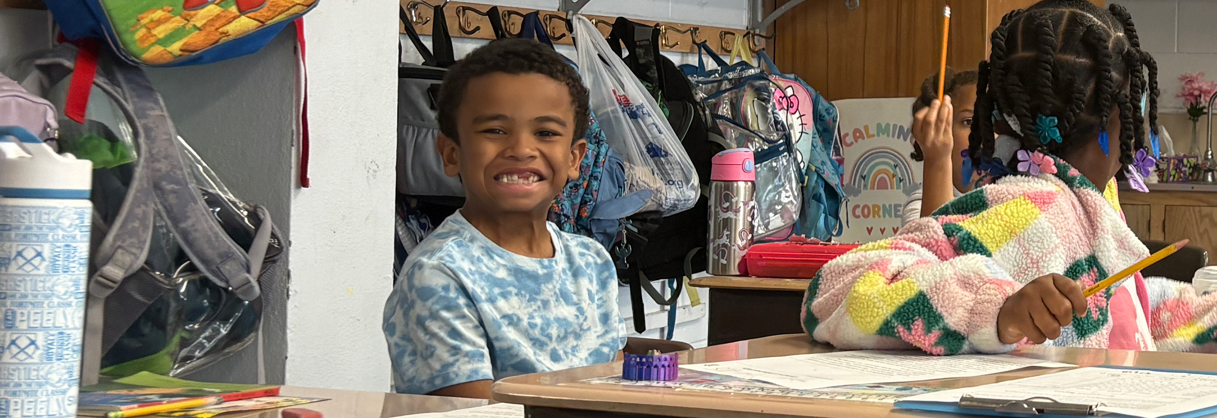 Student sitting at desk with a big smile.