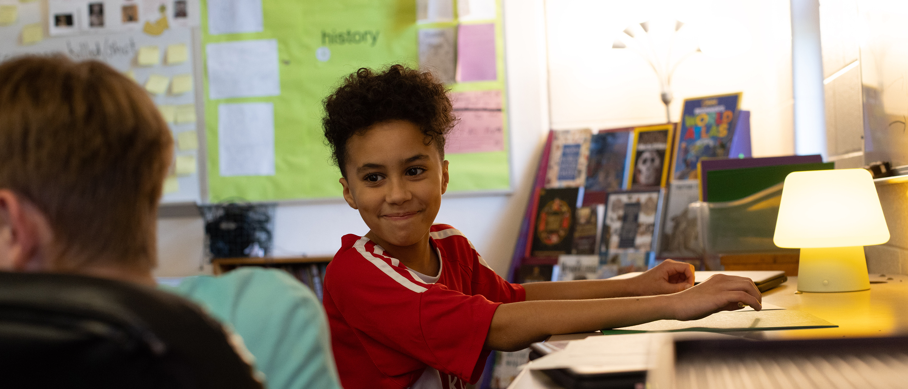 A student in a red shirt and pigtails smiles at a classmate.