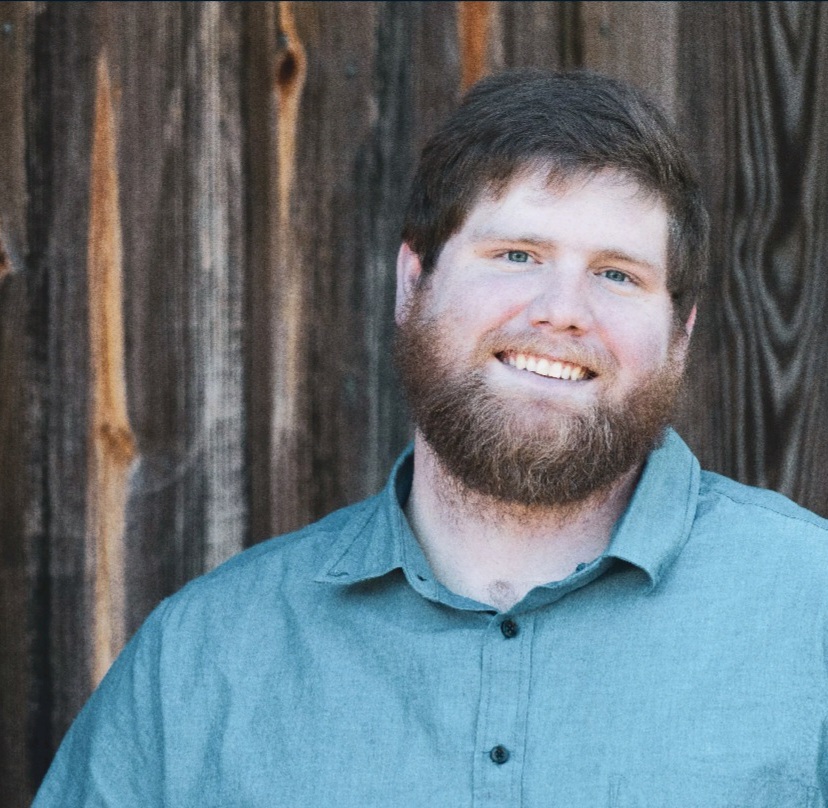 Koltyn Woolverton wearing a blue button up shirt with a wooden fence background