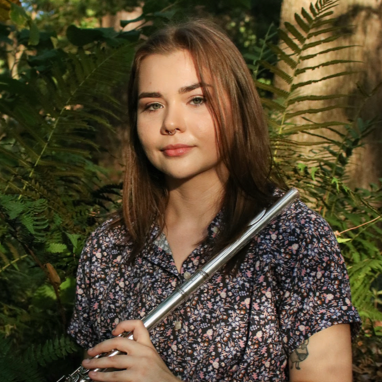 Ms. Sandidge holding her flute with foliage behind 