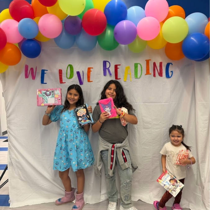 students posing with their book purchases in front of a backdrop that states "We love reading"