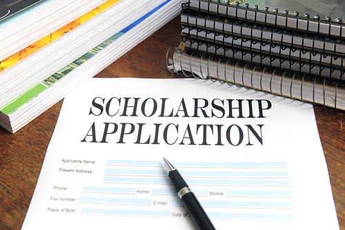 A paper with the words "Scholarship Application" is by the center of a table along with a couple of notebooks and textbooks.