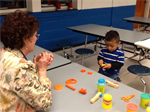 An adult watching a young student play with PlayDoh