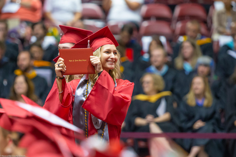 A graduate holding up her diploma as she crosses the stage