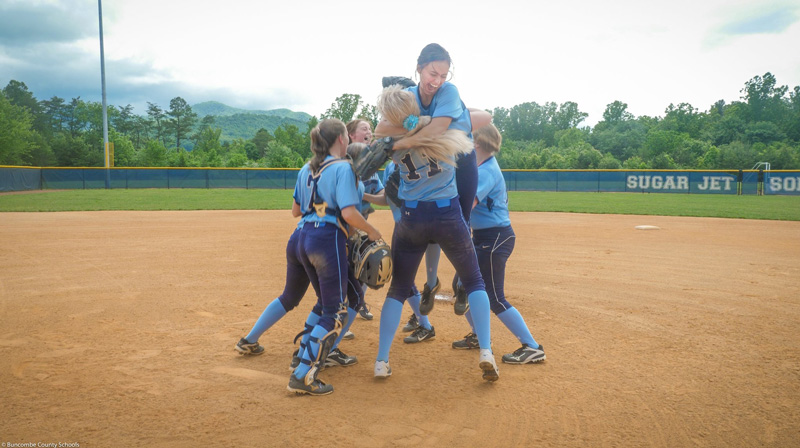 The Enka High Sugar Jets softball team celebrates at the mound.