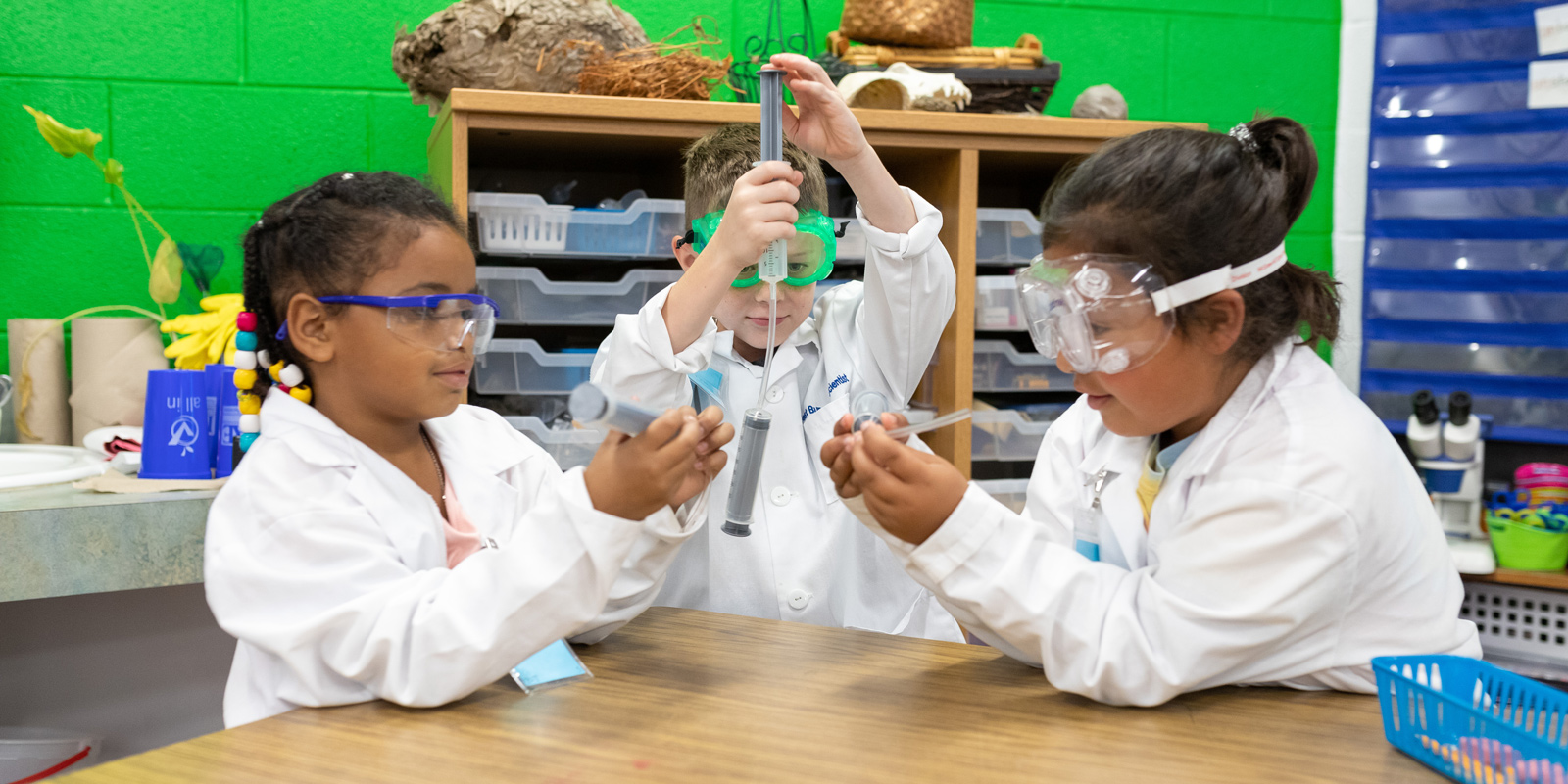 Three students doing an experiment while wearing lab coats.