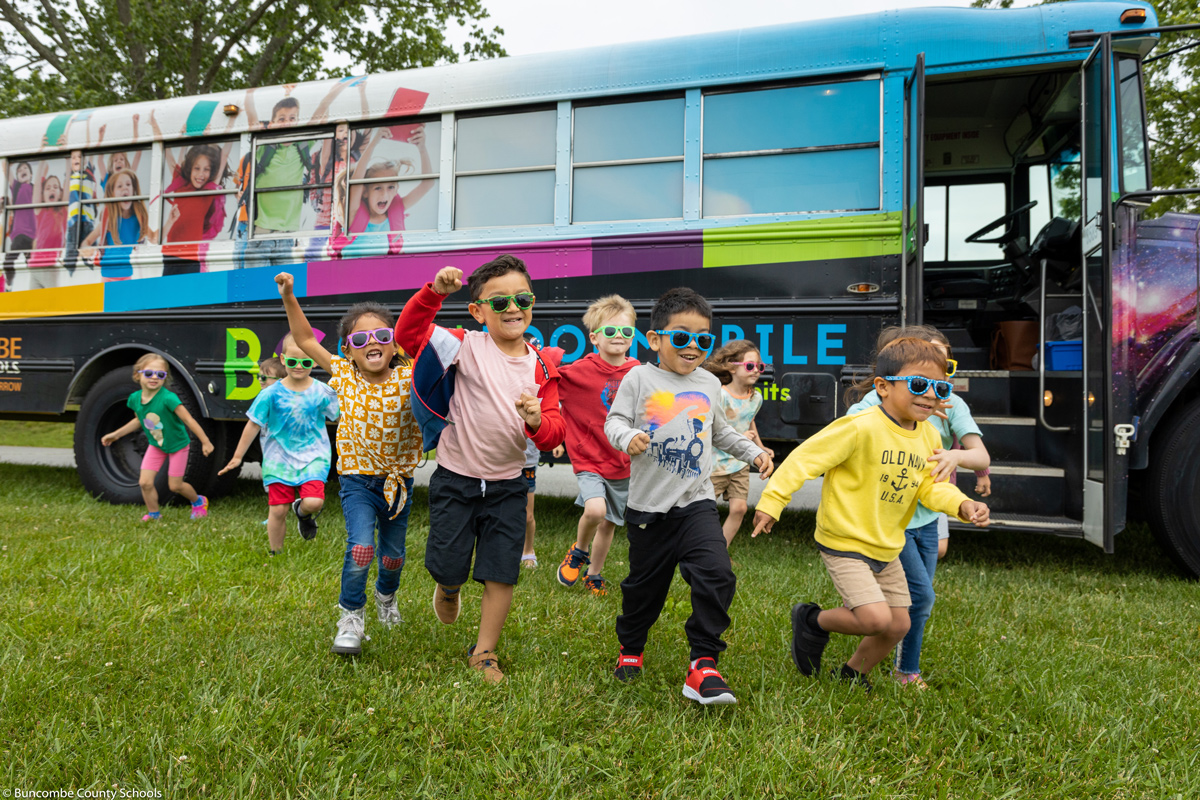 Pre-K students wearing sunglasses and running in front of the Bookmobile.