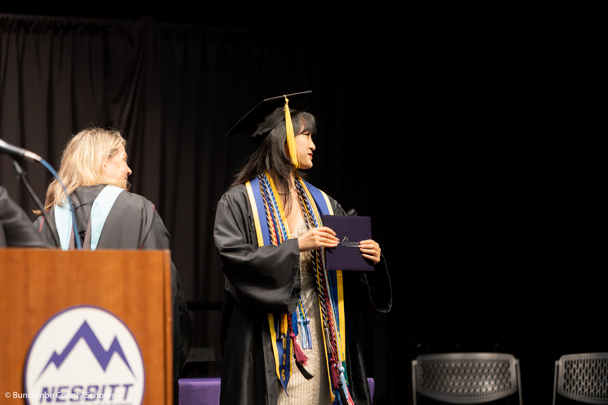 Student standing on graduation stage, holding her diploma. 