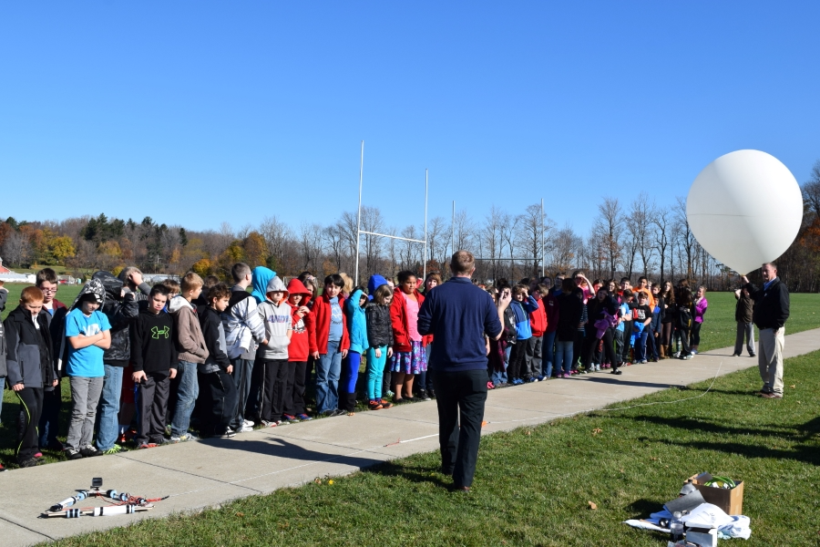 Middle school students standing outside listening to a presenter talk about high altitude weather balloons