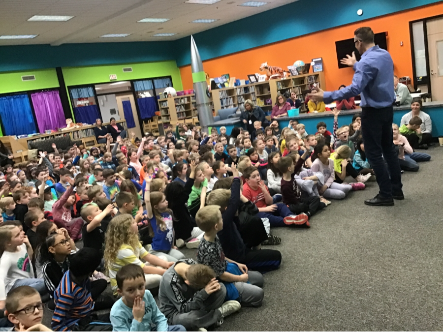 Elementary students in the library listening to a presenter