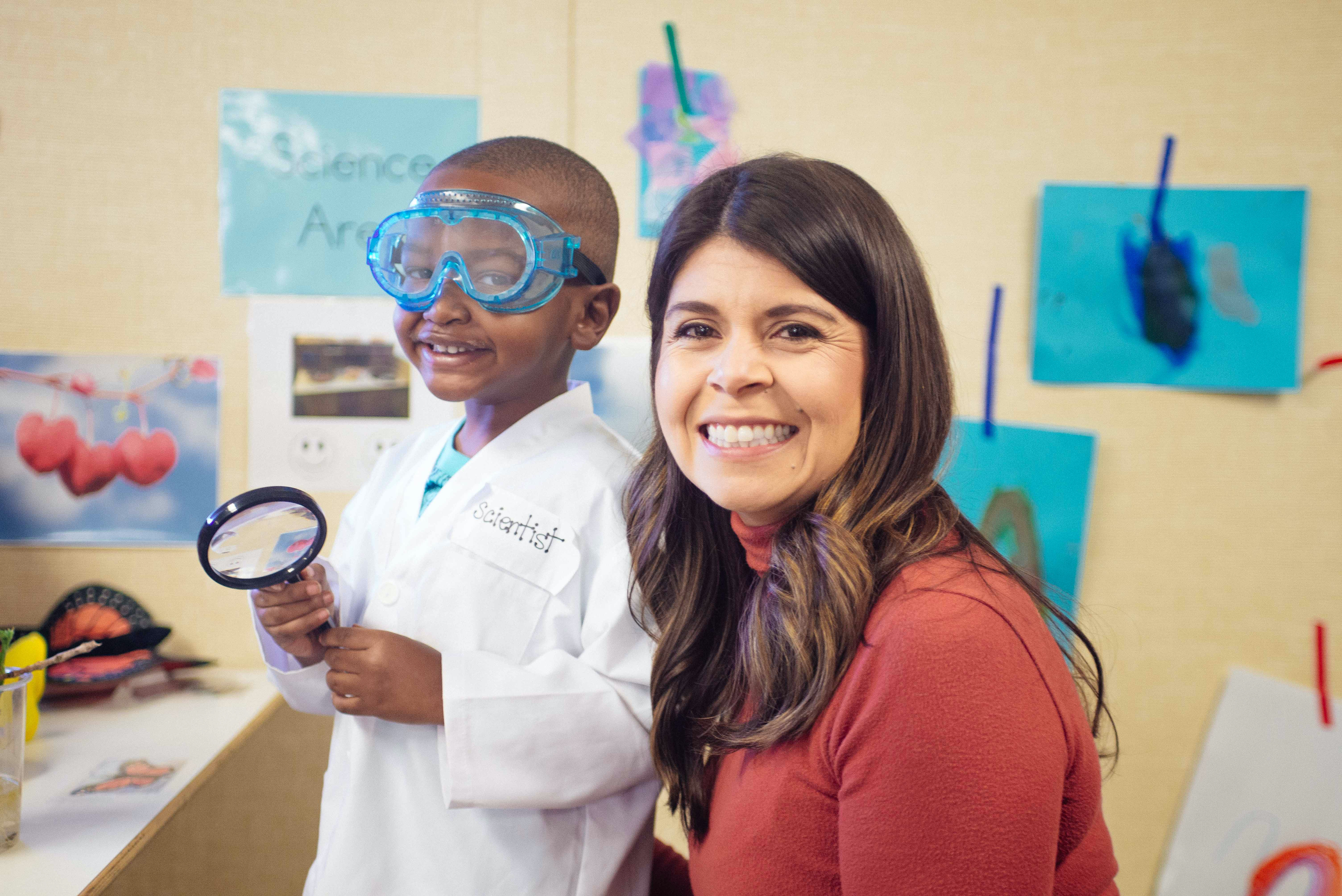 preschooler wearing lab coat, goggles with teacher