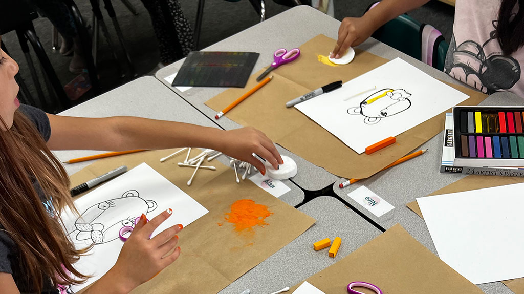 Students working on drawing and painting art project at desks.