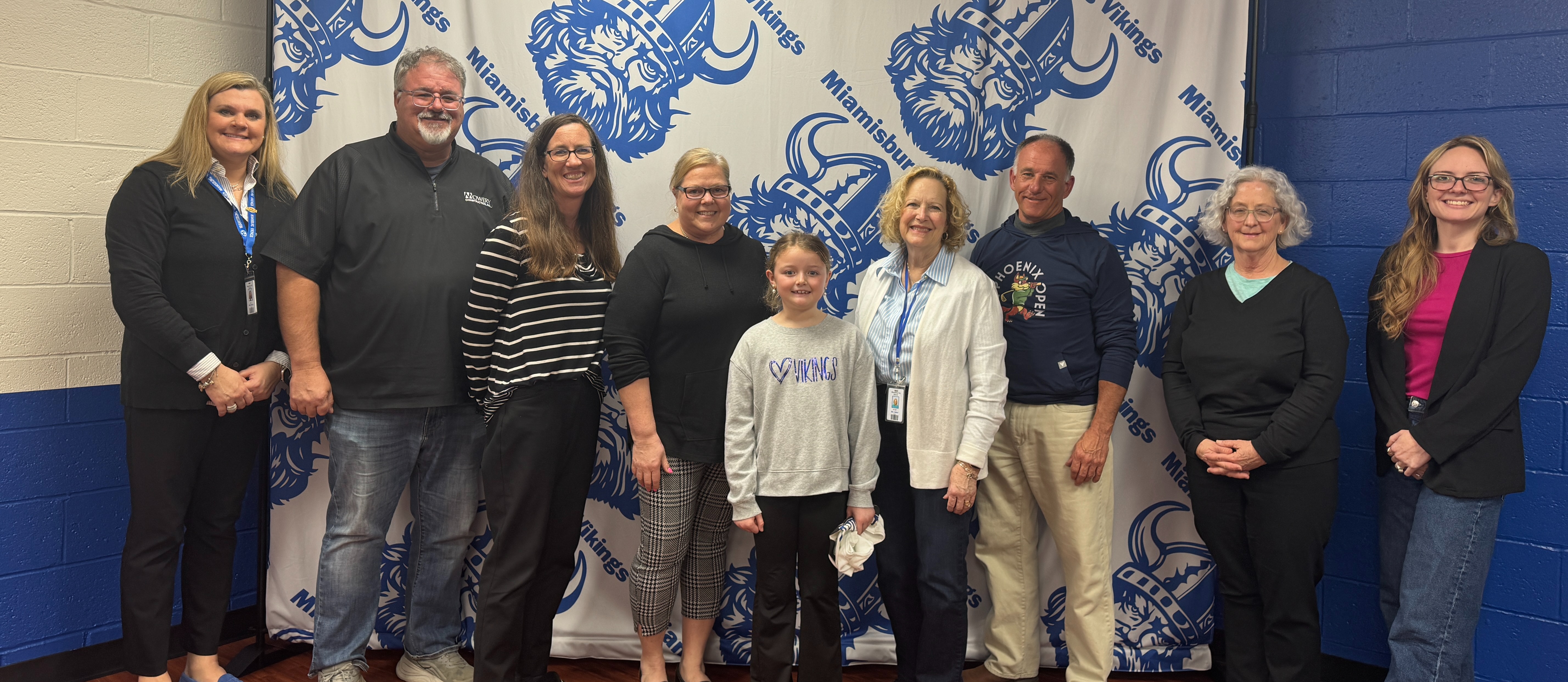 Nine adults and a child standing in front of a white and blue backdrop with blue and white graphics.
