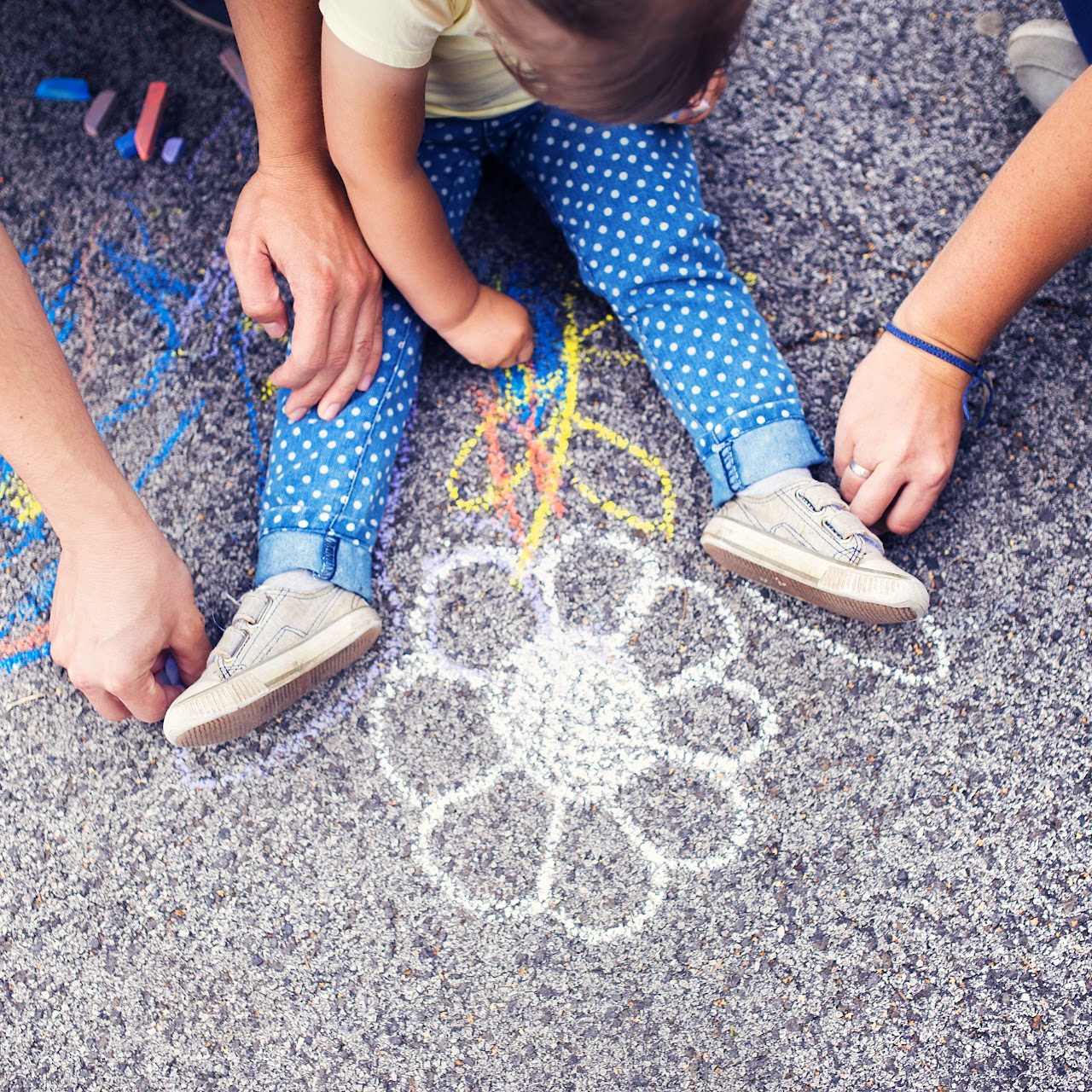 Little Girl and two adults drawing a flower on the sidewalk 