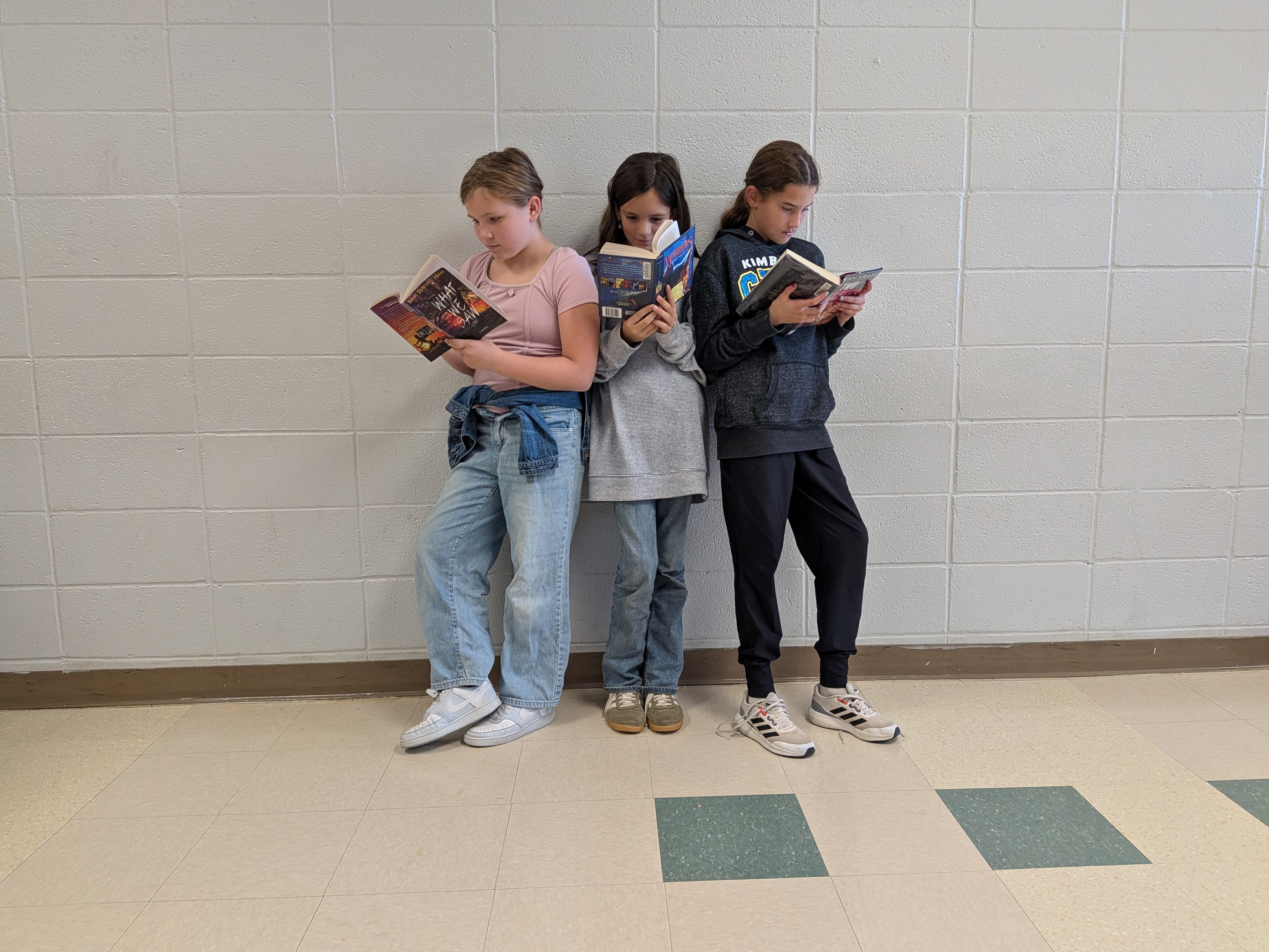 three 6th grade girls reading books while standing in line for lunch