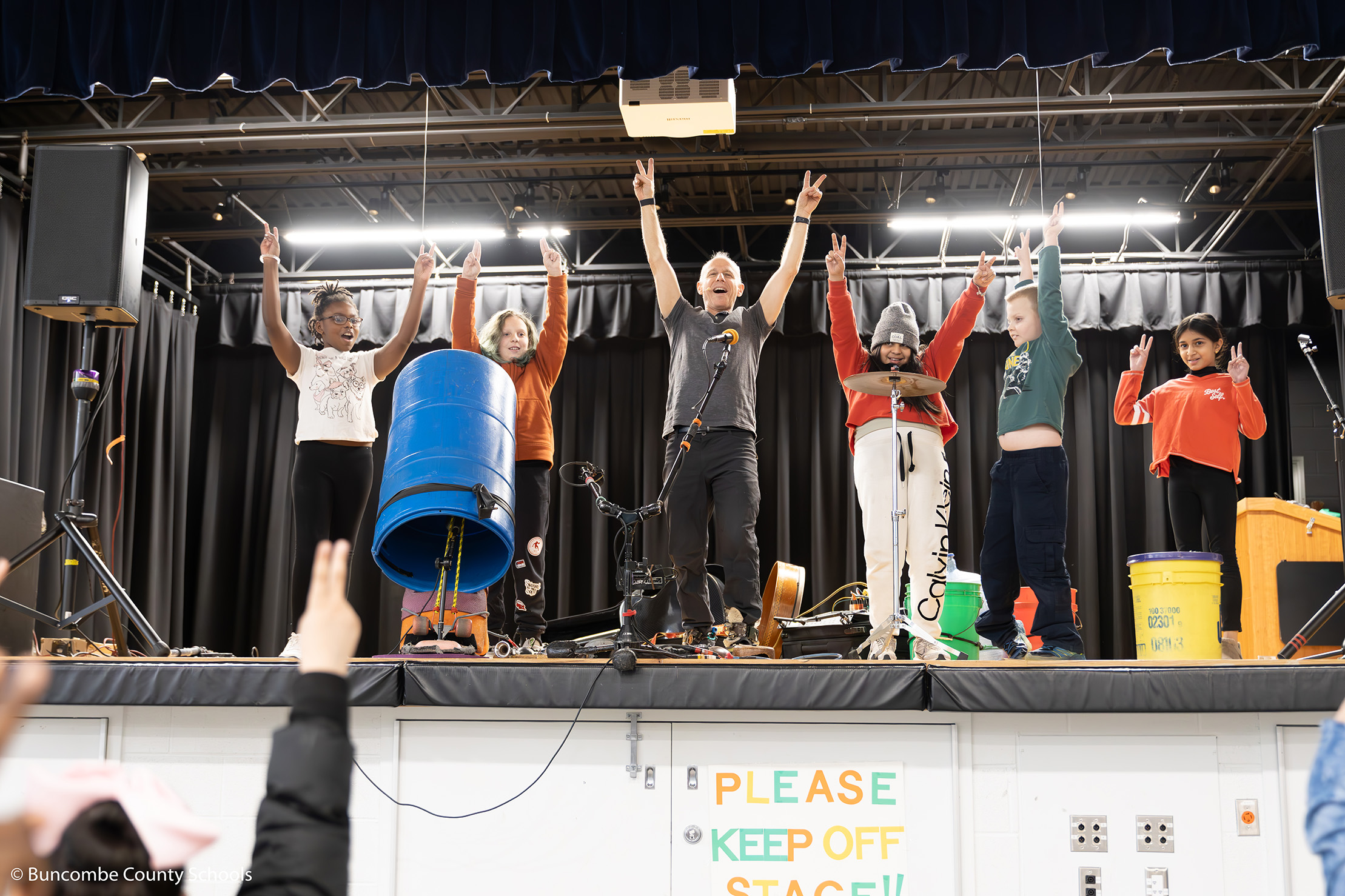 Billy Jonas surrounded on either side of the stage by students who played an instrument, and just finished a song with their hands up in the air. 