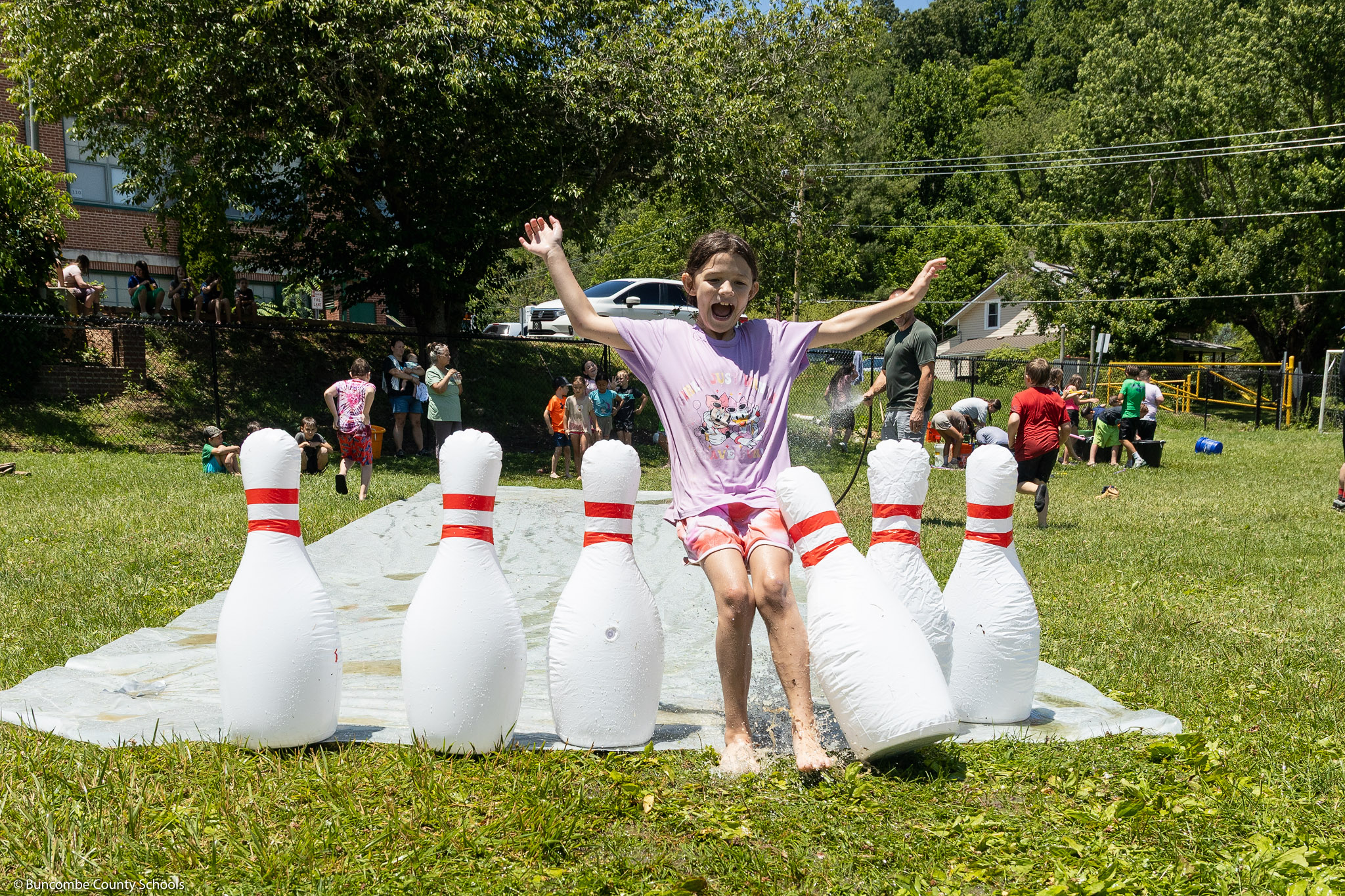A girl runs into inflatable bowling pins on a slip-n-slide.