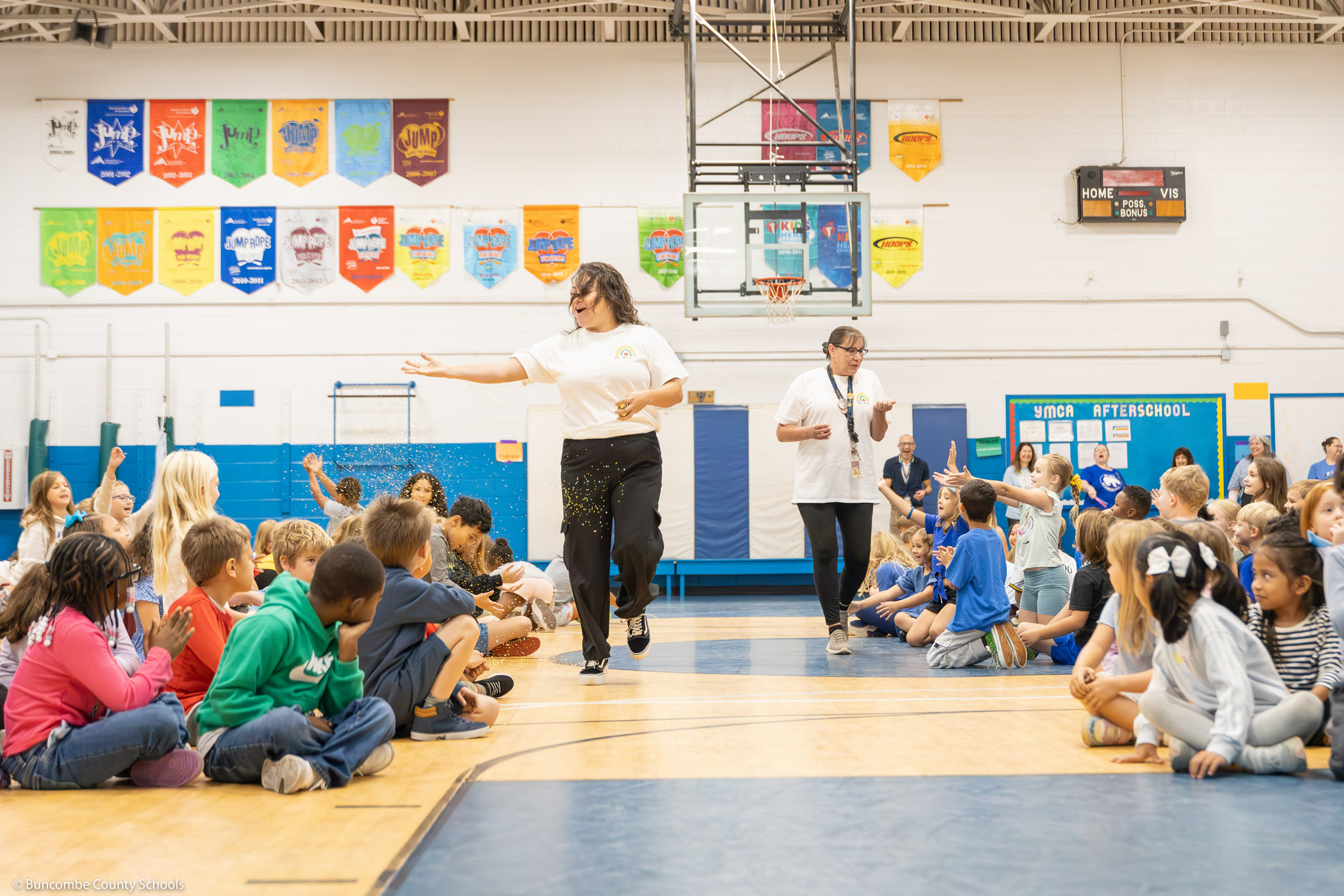 Two teachers throw confetti at a school assembly.