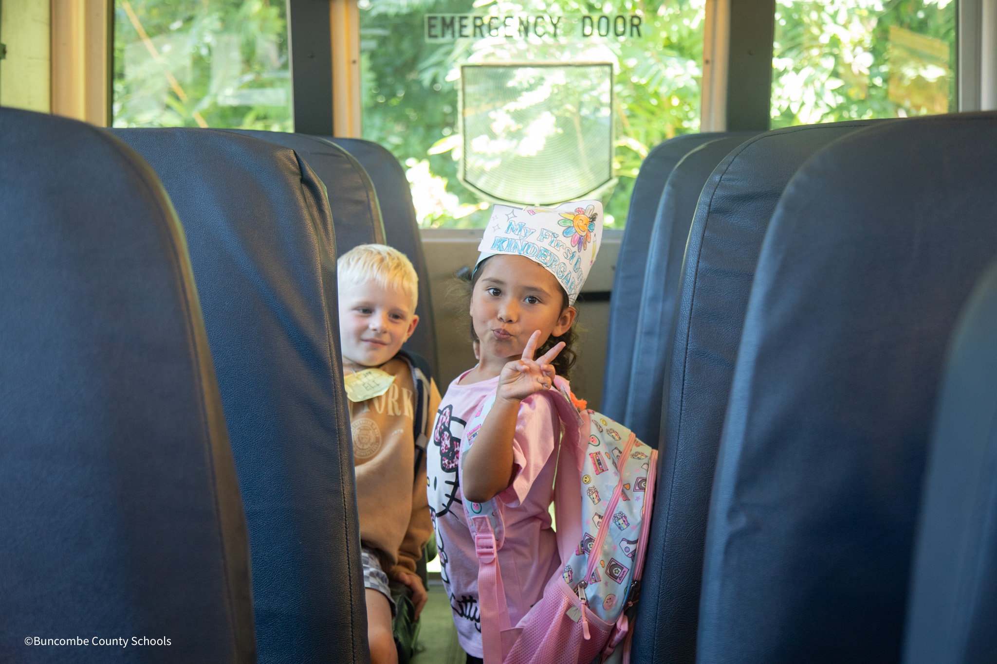 Little girl getting on the school bus and giving the peace sign with her fingers. 