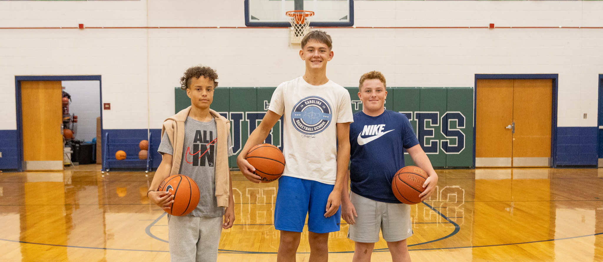 Three boys in the gym, each holding a basketball. 