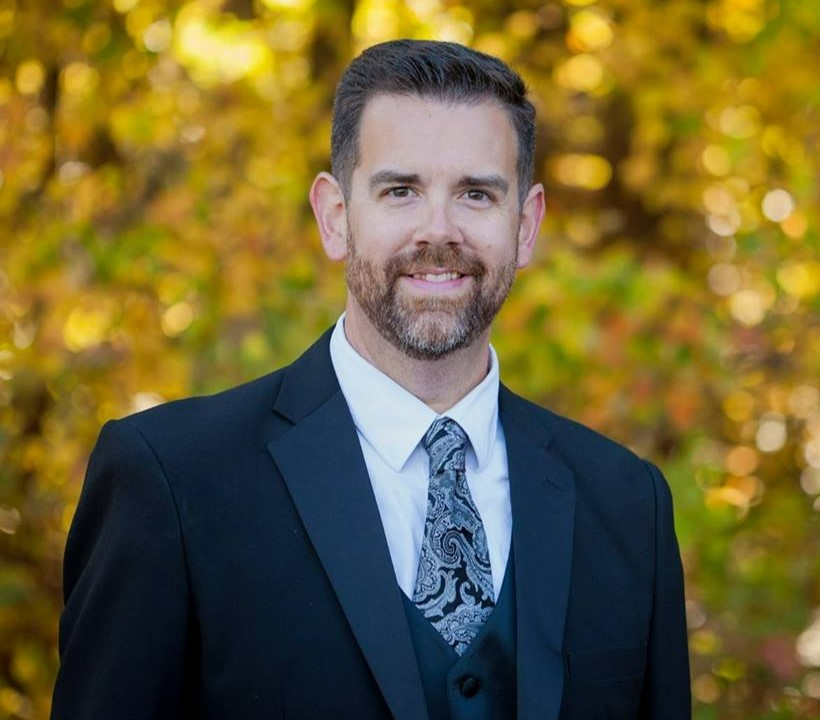 photo of Choral Director Phillip Haynie smiling in front of fall foliage