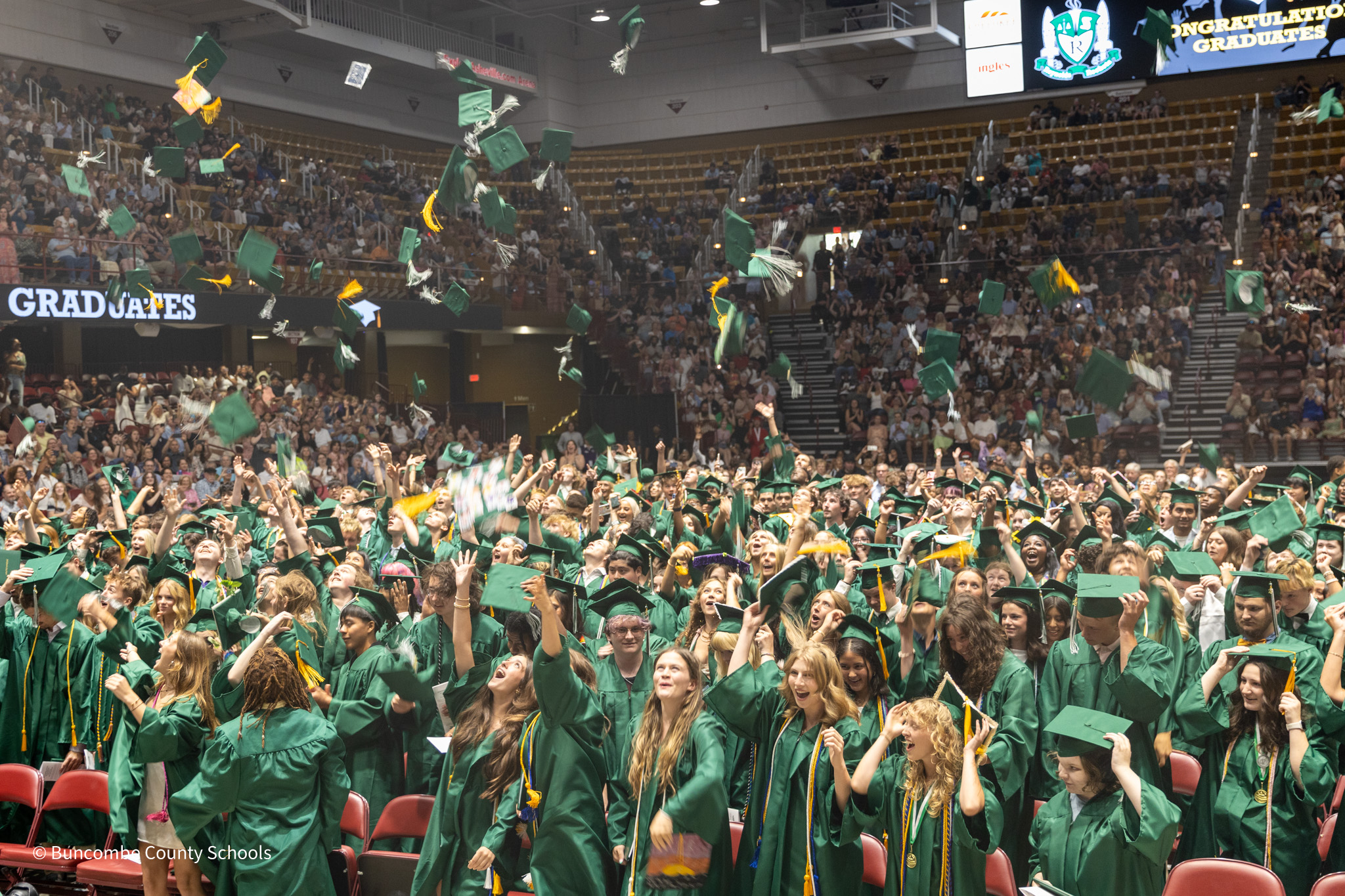 Graduates in green gowns toss their green caps into the air.