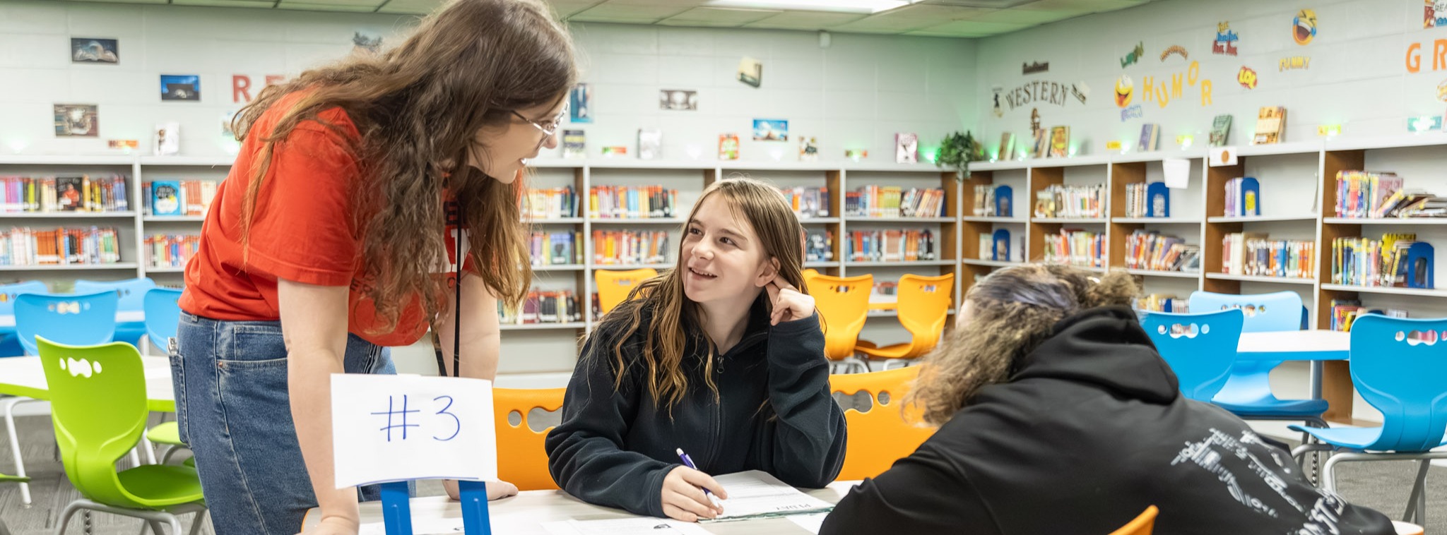 A student smiles while talking to a teacher in the media center.
