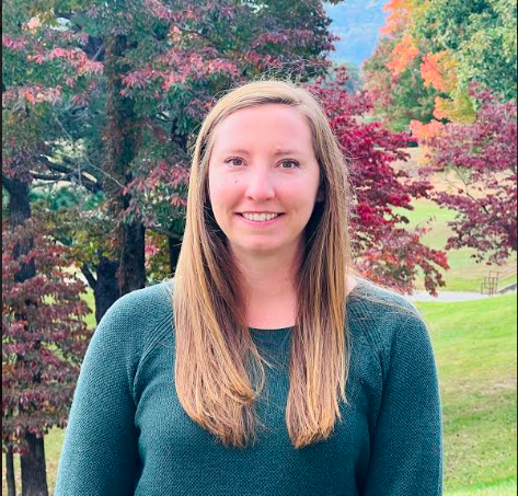 This is a picture of Ms. McIntosh in front of beautiful autumn trees.