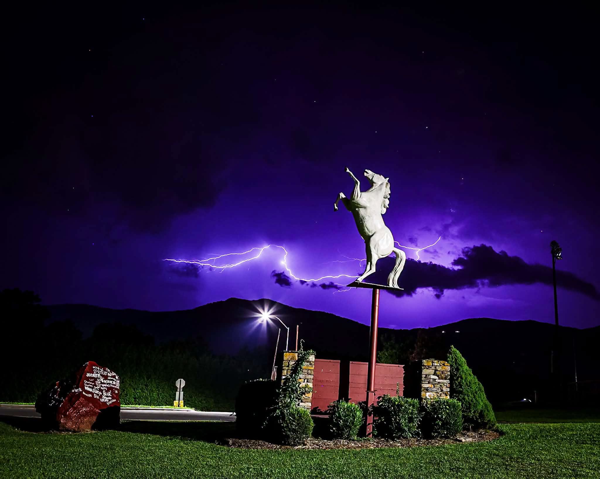 Photo of a night sky with lightning striking and the Owen Warhorse statue in front of the lightening. 