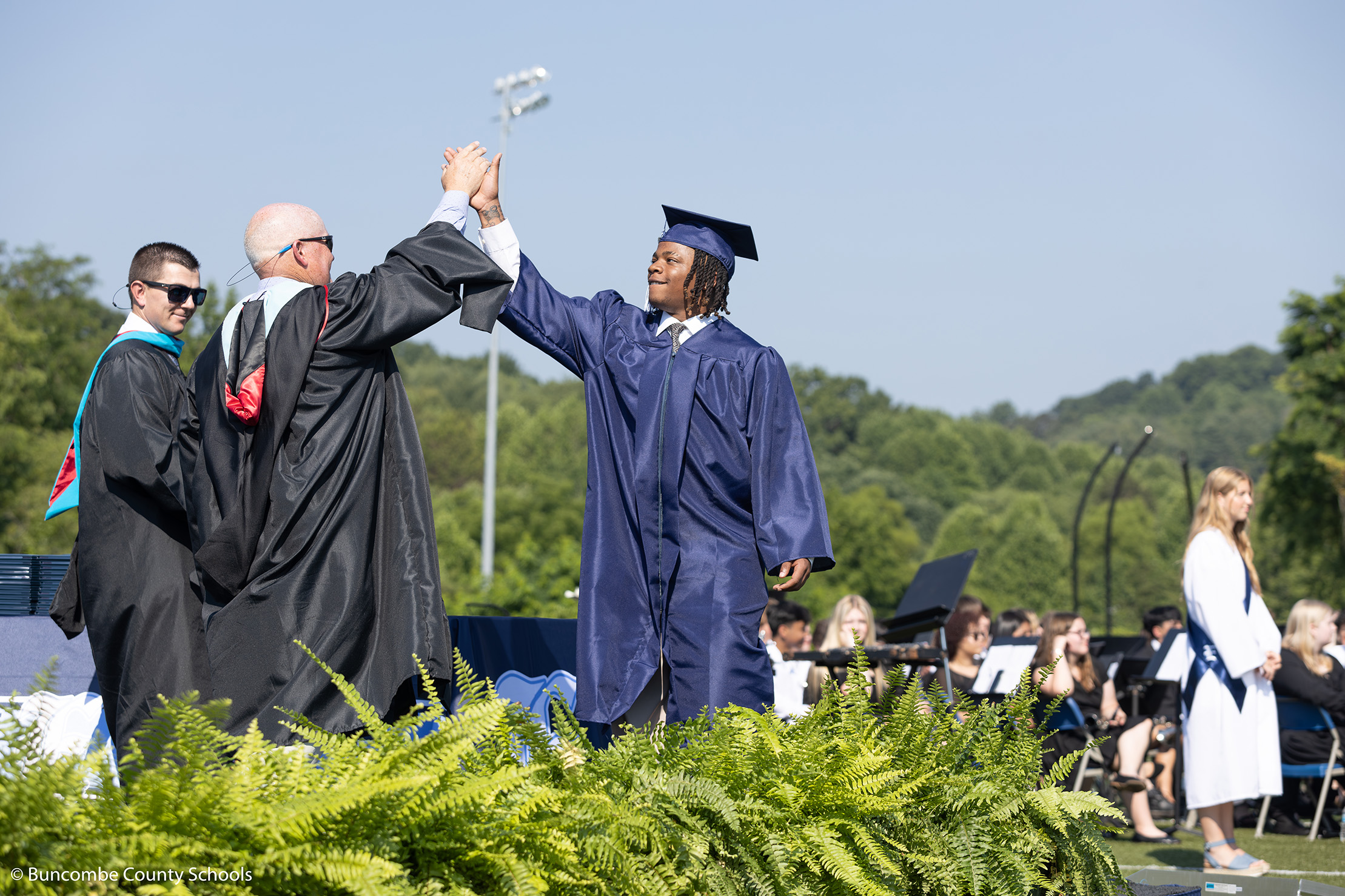 Male student walking across the stage at graduation giving Principal Jeffery Burleson a high five. 