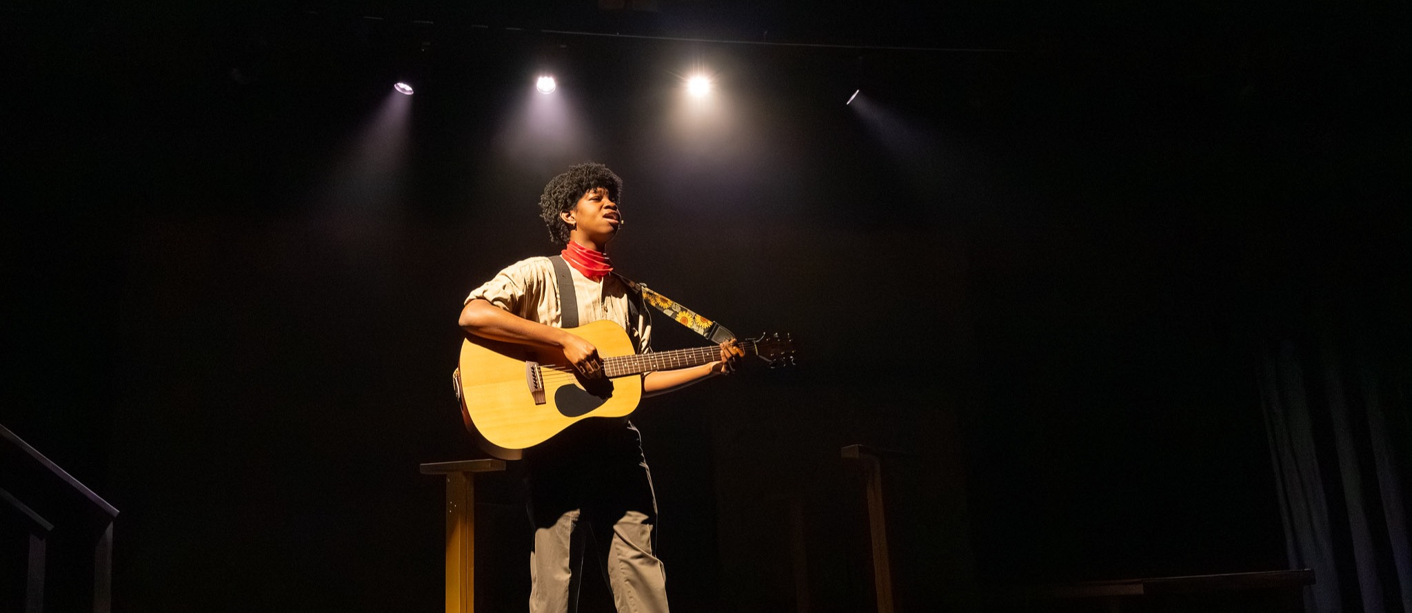 A student wearing a costume and holding a guitar plays on stage during the 2026 "Hadestown" dress rehearsal.