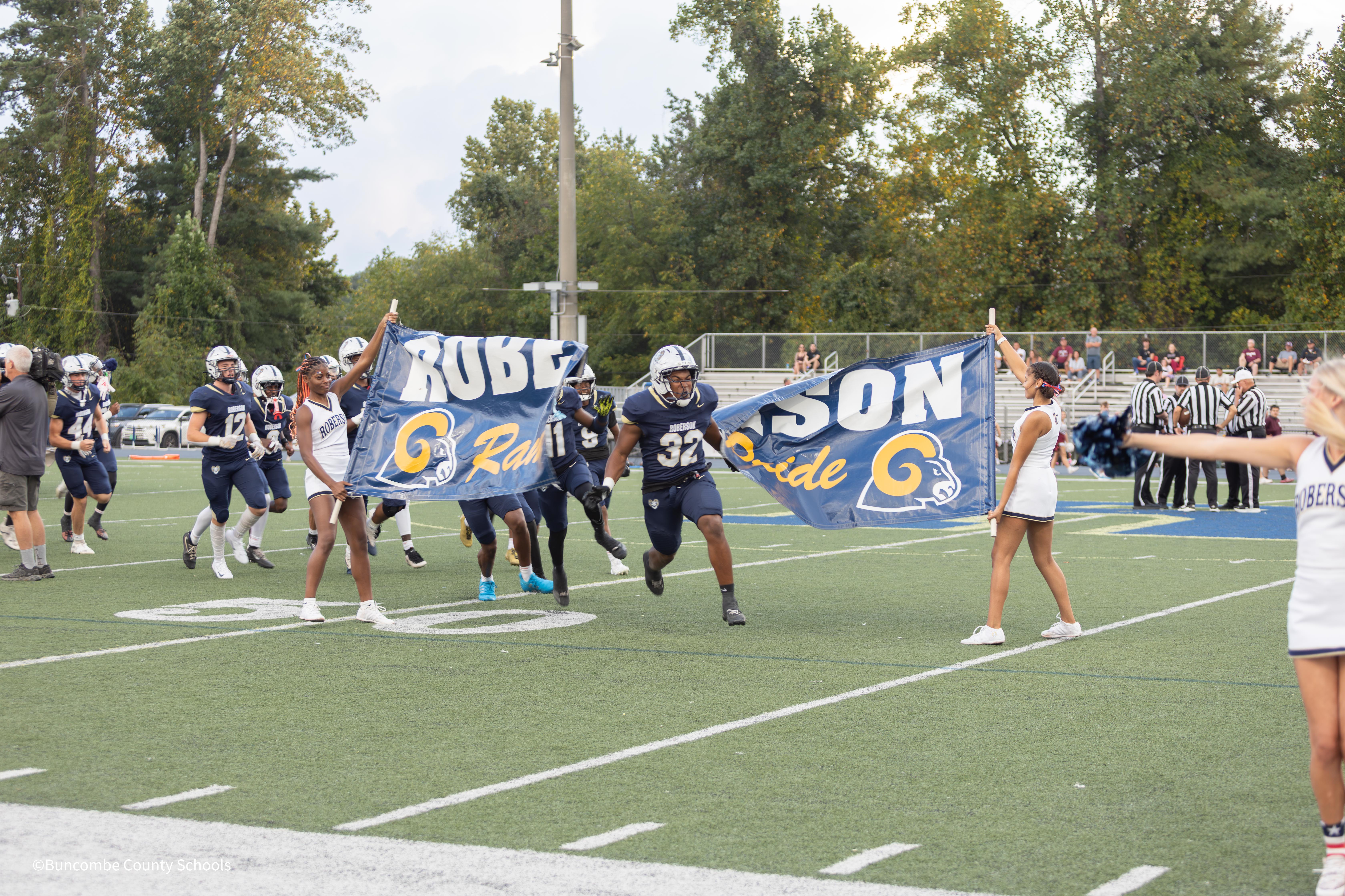 football players run through banner