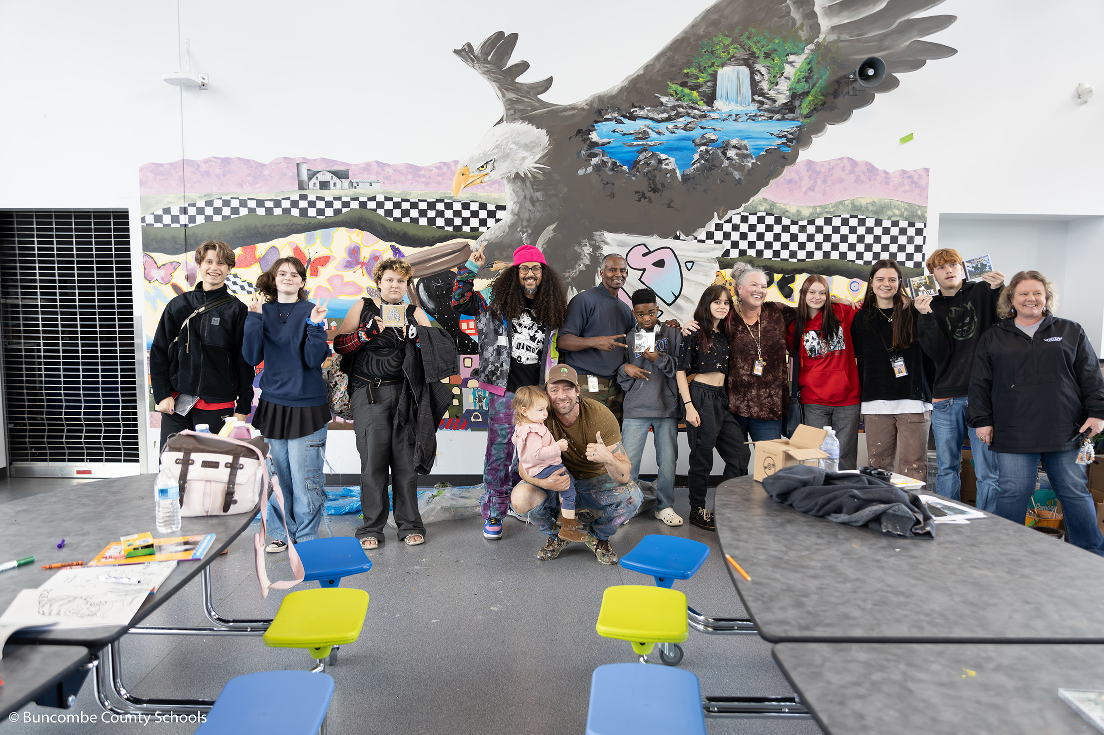 The students, staff and artists standing in front of the mural in the cafeteria for a photo. 