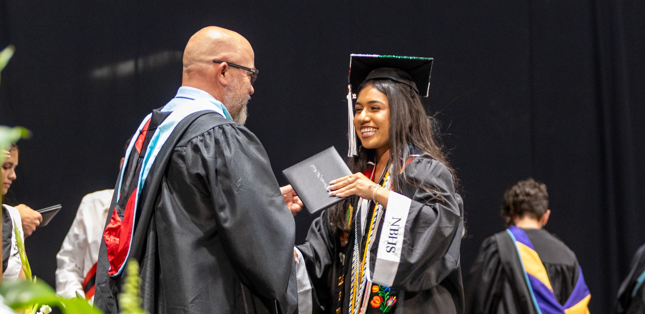 The principal shakes hands with a graduate in a black cap and gown