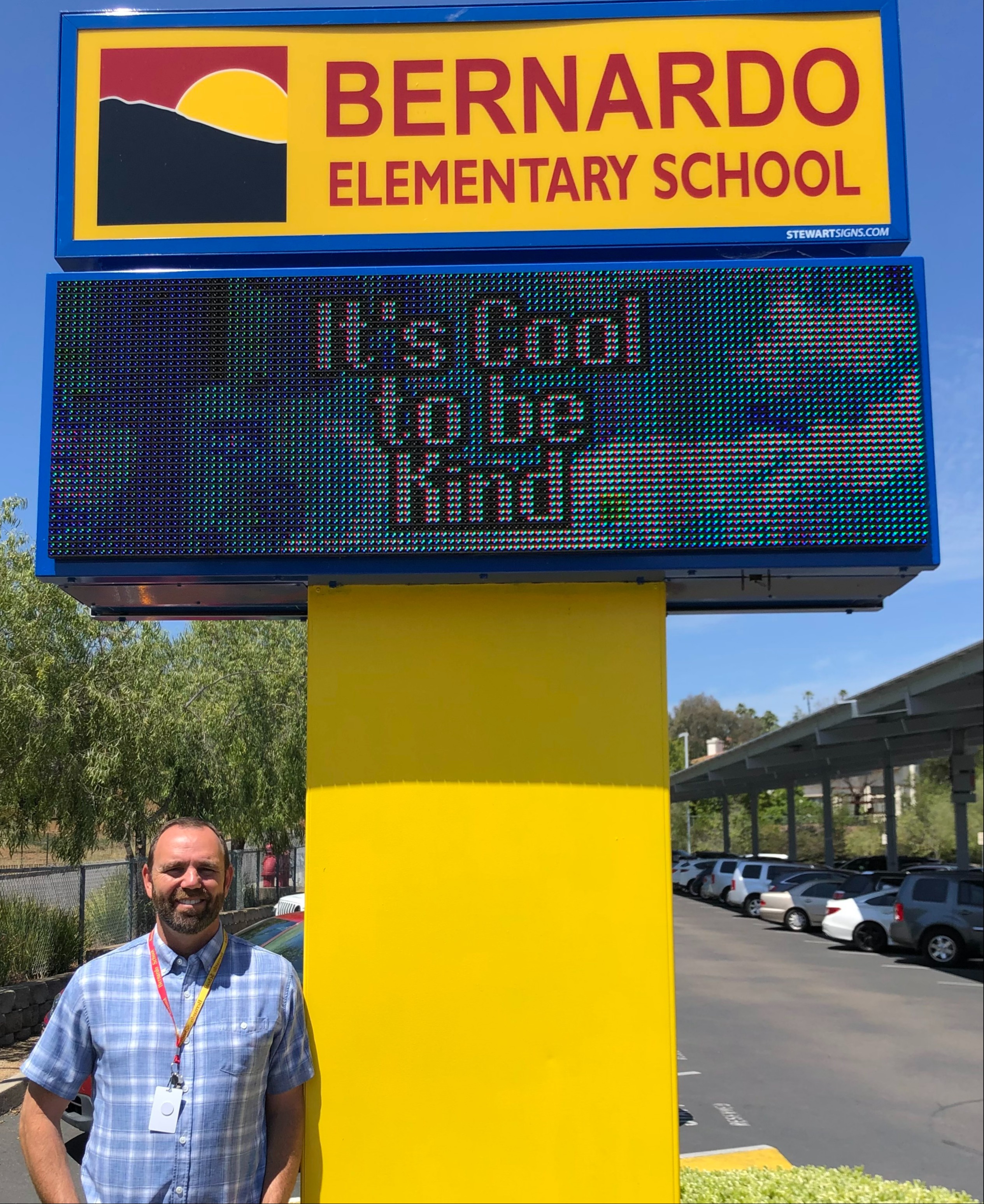 Principal Jeremy Lyche standing next to the Bernardo marquee with the message It's Cool to be Kind.