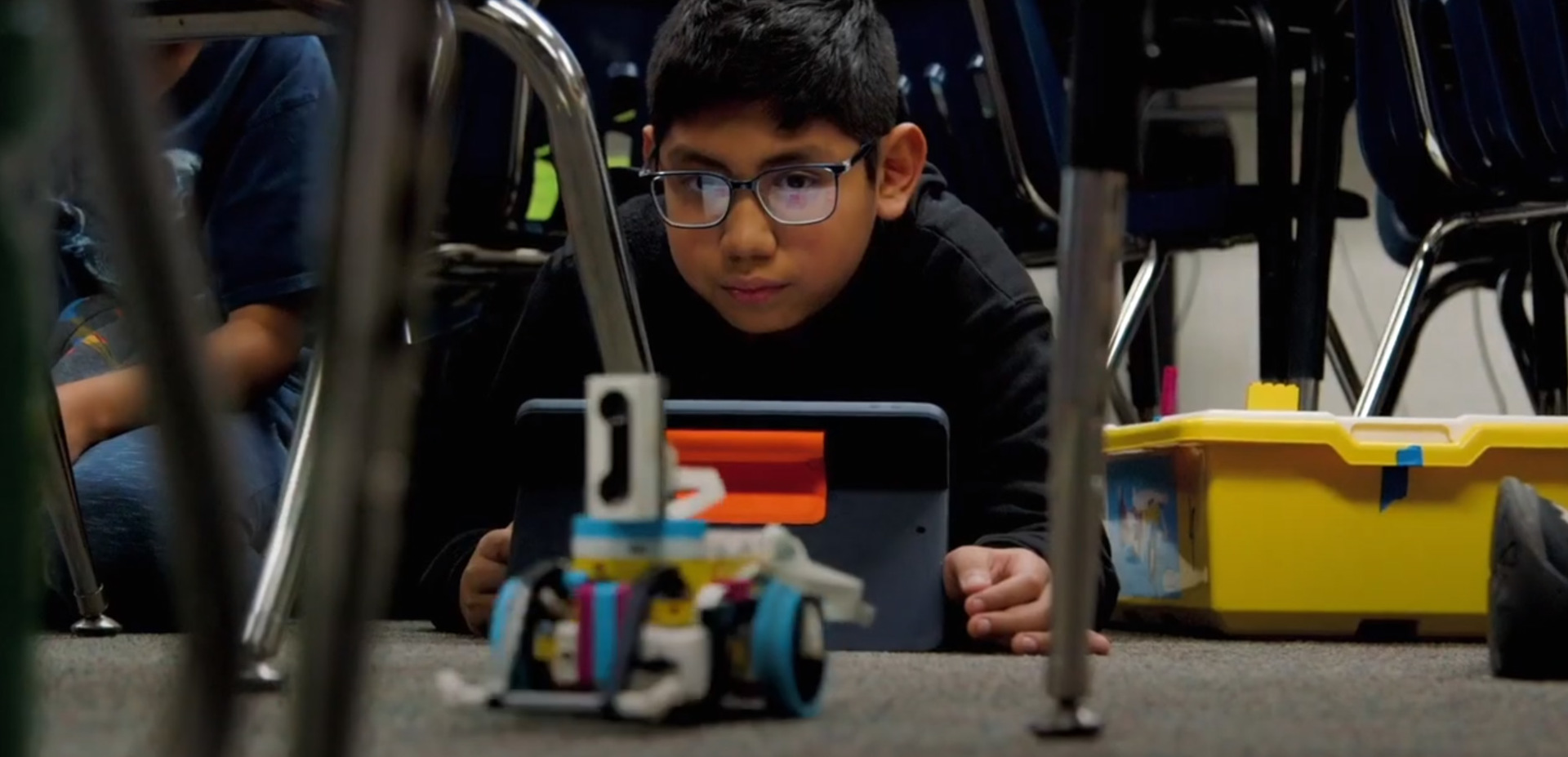 Student with iPad and Lego robot on classroom floor