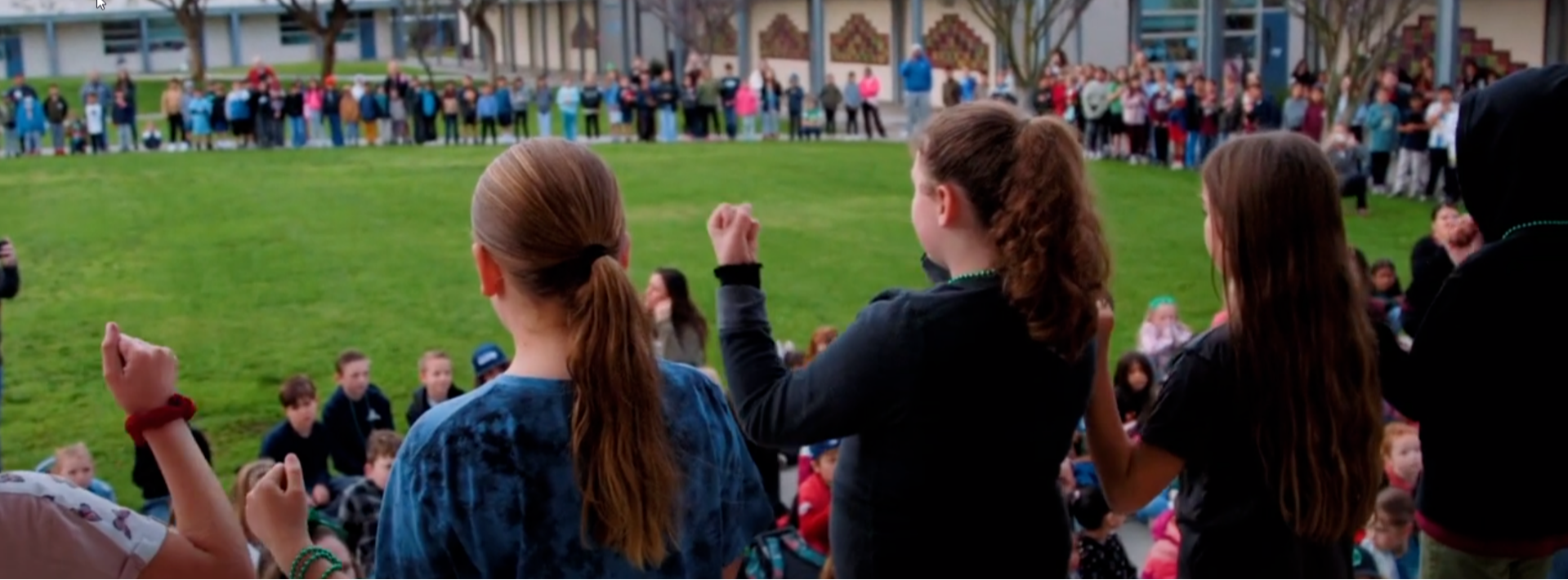 Reidy Creek students gathered outside and singing the national anthem while several students provide sign language.