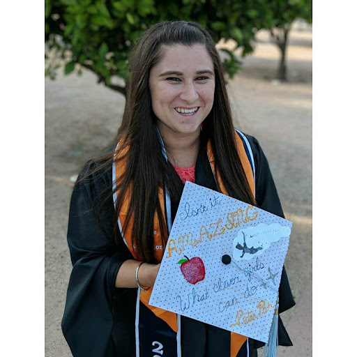  A woman proudly holds her graduation cap while wearing a graduation cap and gown.