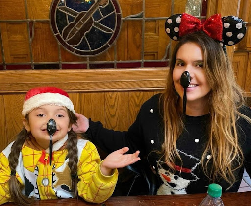 A female adult and a young child donning Mickey Mouse ears, sitting side by side with a spoon balancing on each of their respective noses.