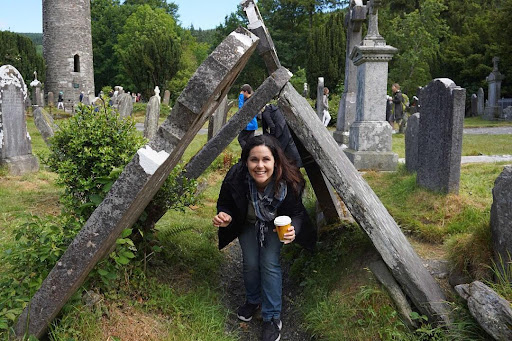 A woman crouches underneath a sturdy wooden structure while holding a coffee cup.