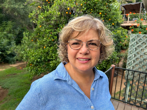 A woman with glasses standing in front of an orange tree.