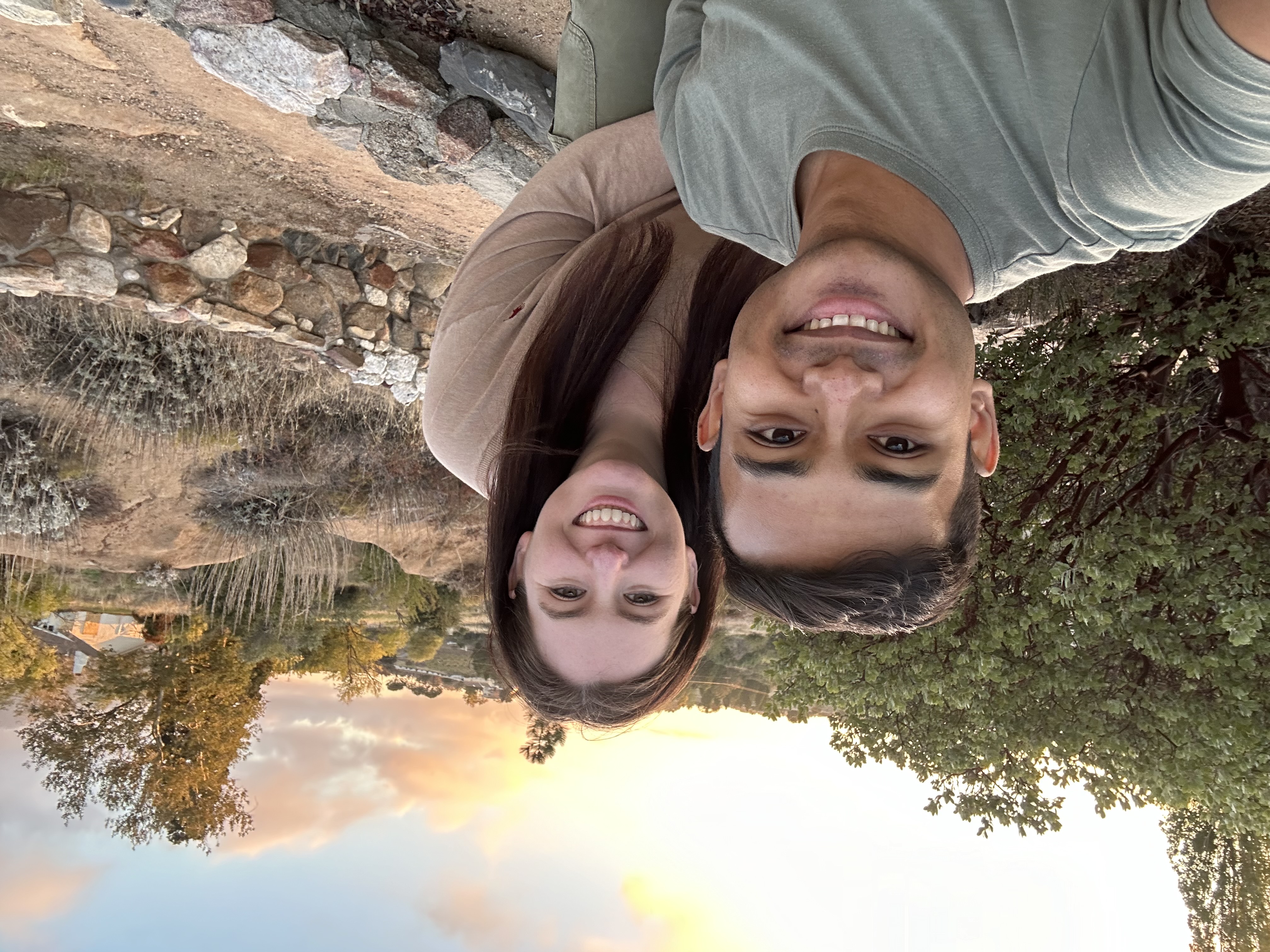 a man in a gray shirt and woman in a beige top smiling at the camera in nature