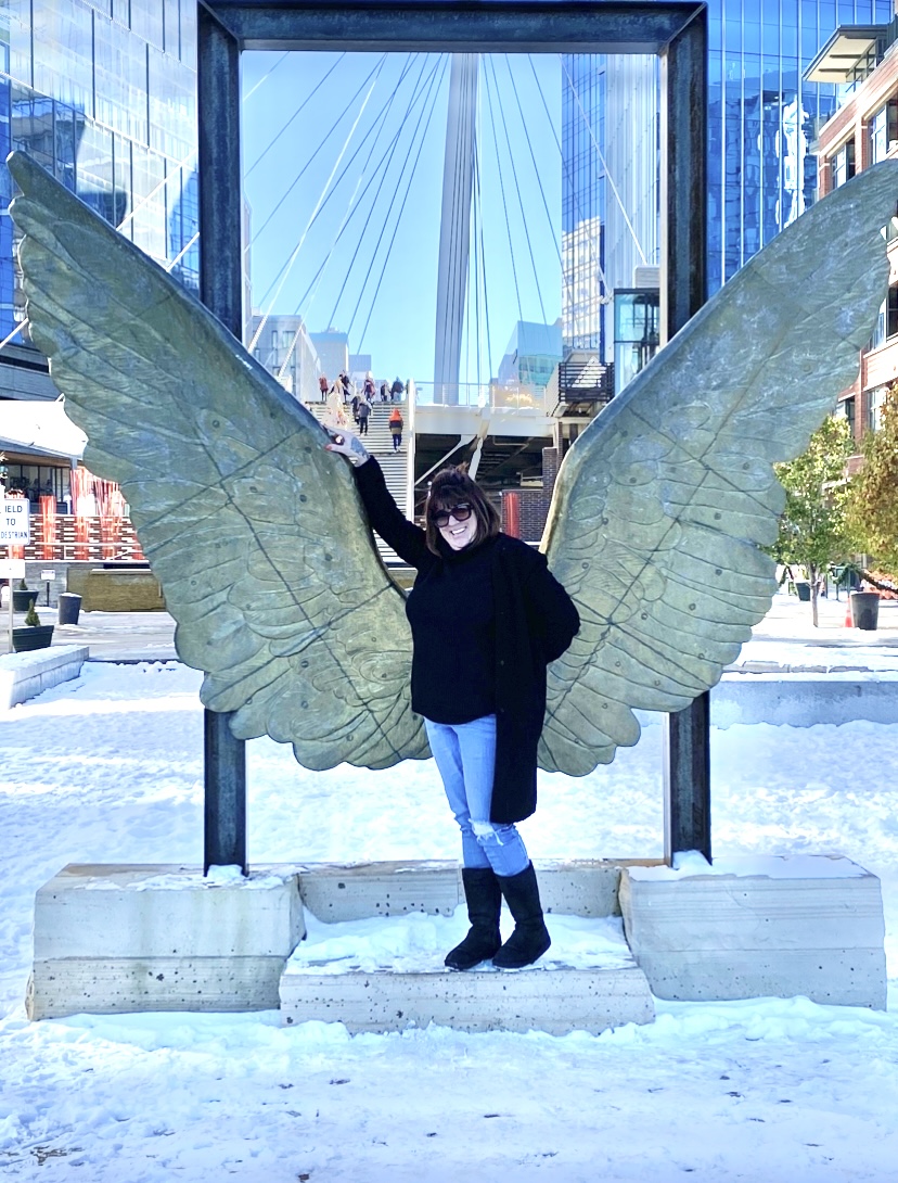 a woman in a black top and black boots posing in front of wings